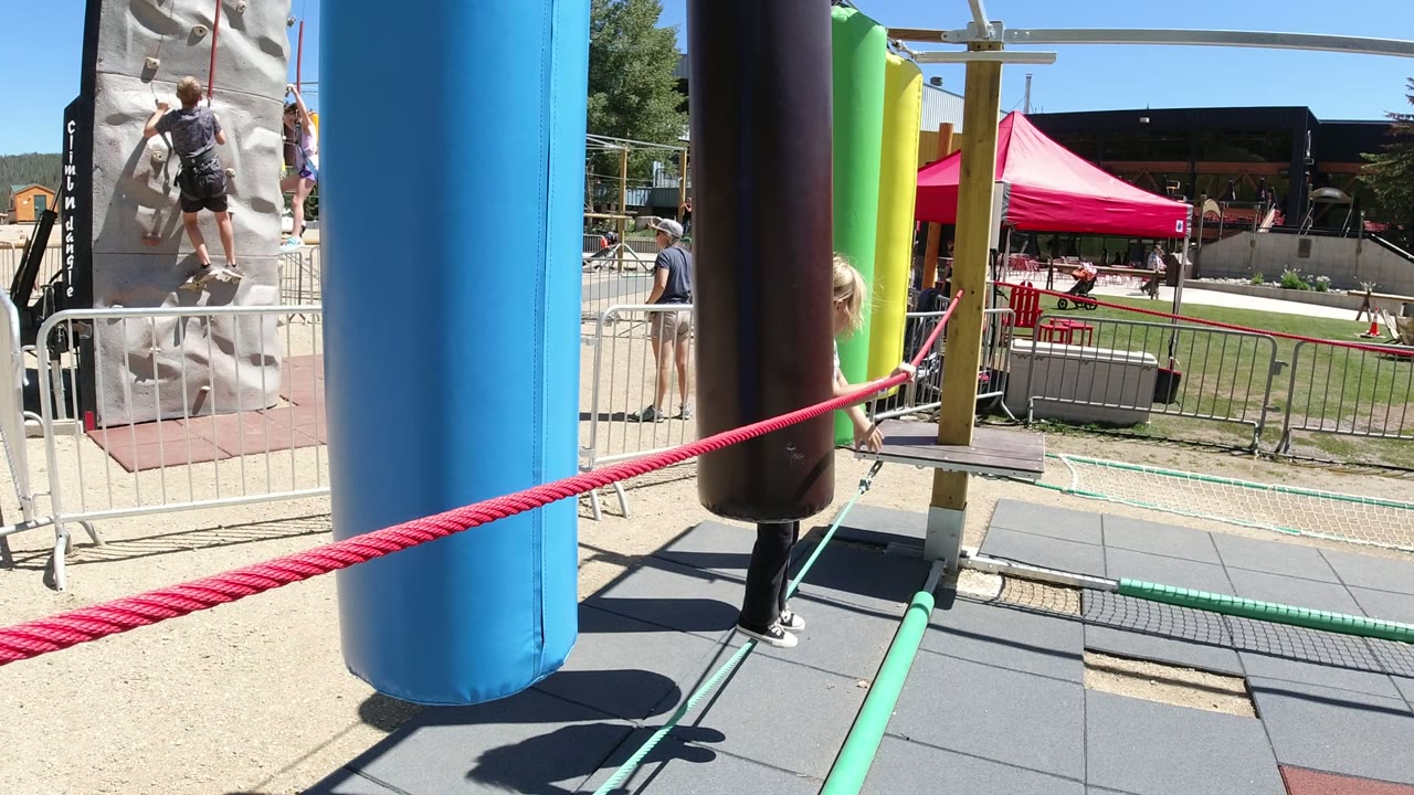 Girl balancing on a rope beside colorful hanging pads at an outdoor play area.