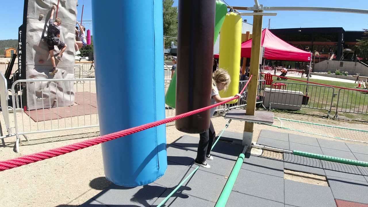 At Winter Park, Colorado, the girl is partly obscured by the blue and brown hanging pads as the rope runs diagonally across the foreground and the activity area remains visible behind.
