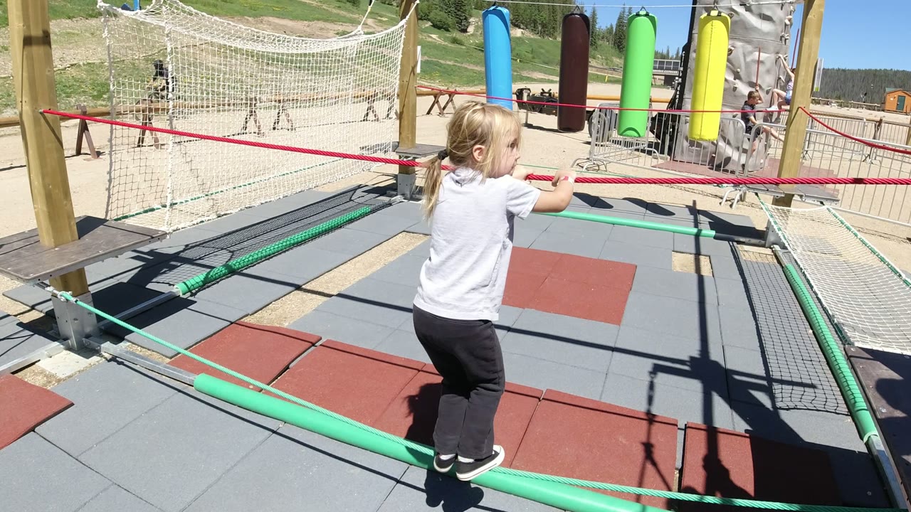 Young girl balancing on green ropes at an outdoor playground.