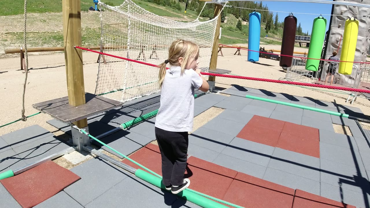 Young girl balancing sideways on green playground ropes.