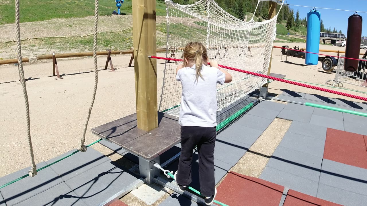 Young girl approaches a rope-and-net playground obstacle.