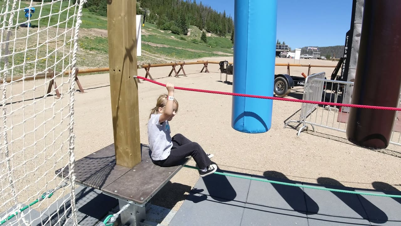 Young girl sitting on a ropes course platform holding a red rope.