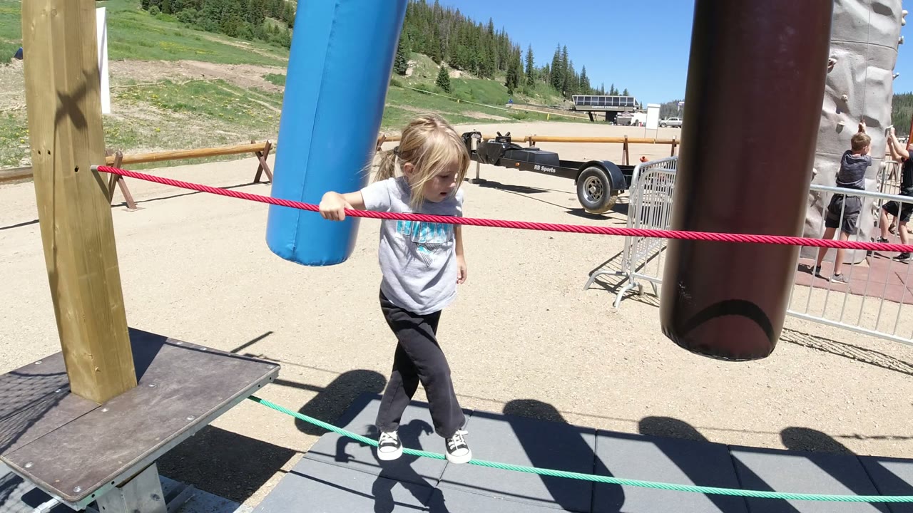 Blonde child holding a red rope between hanging playground tubes.