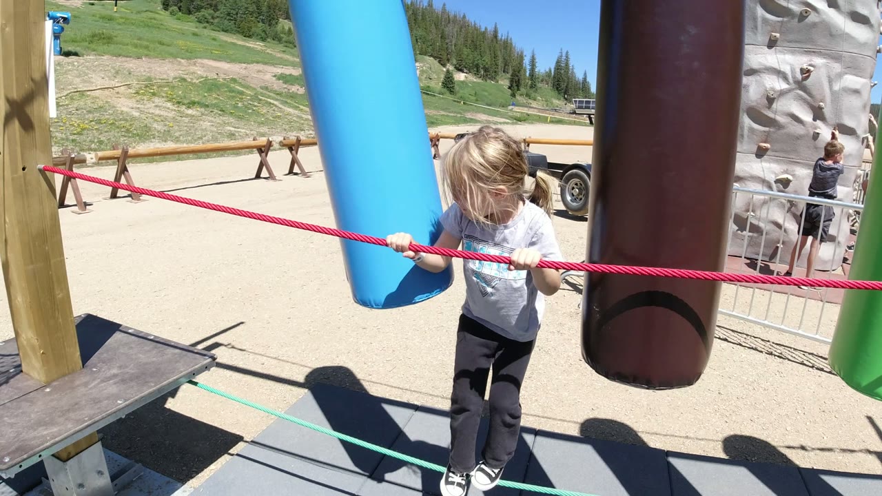 The child leans forward on the suspended ropes in Winter Park, Colorado, with a blue tube close to the body and a brown tube partly blocking the right side.