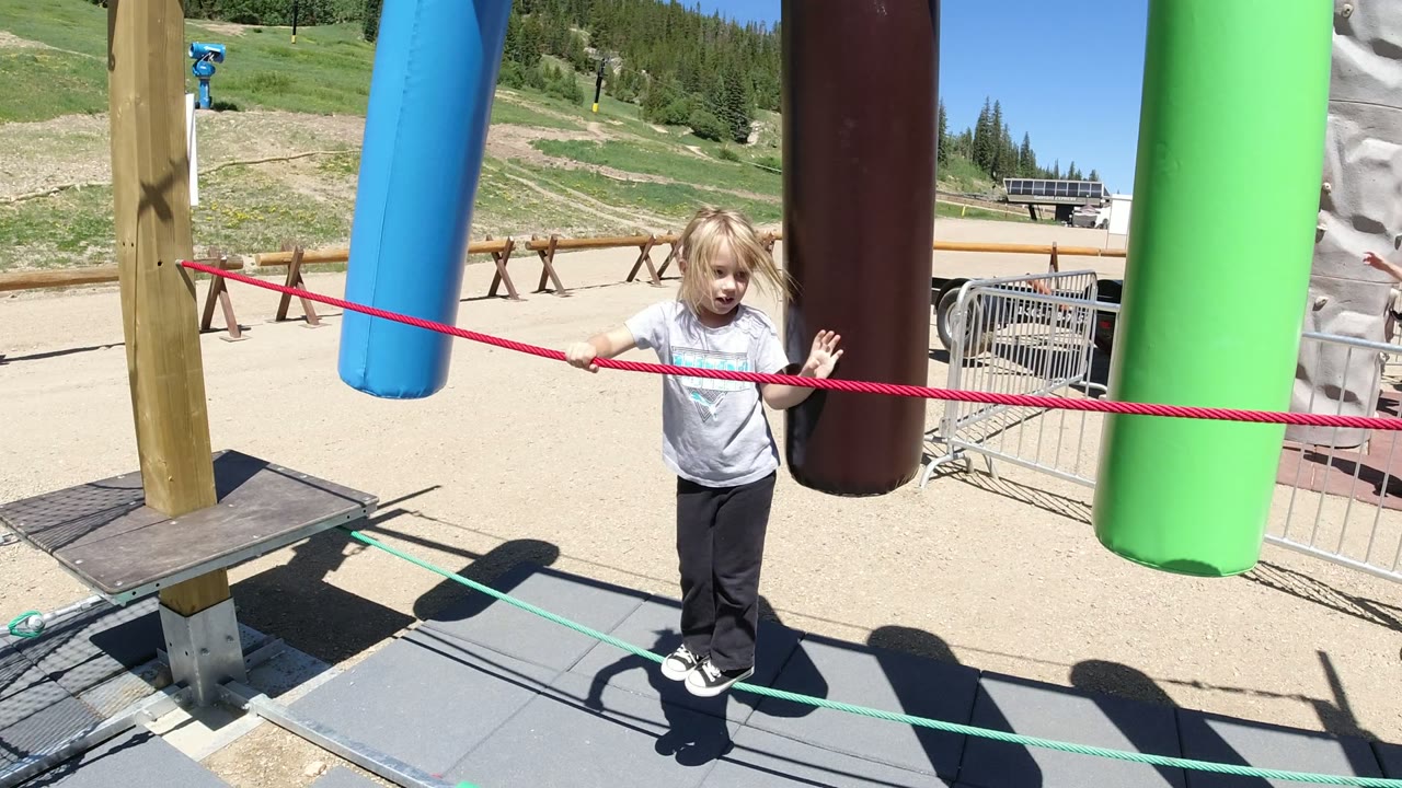 Child balancing on ropes beside hanging foam cylinders.
