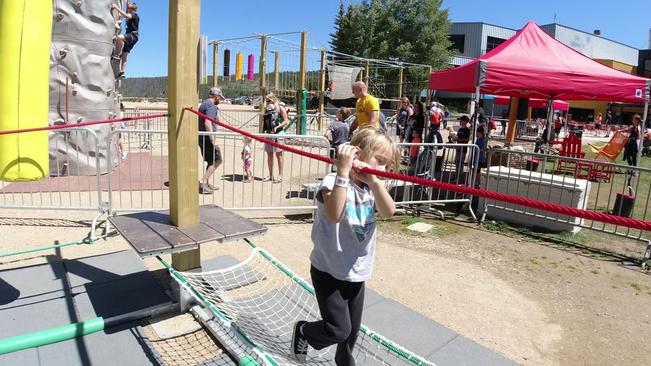 Child holding a red rope beside a net obstacle at an outdoor ropes course.