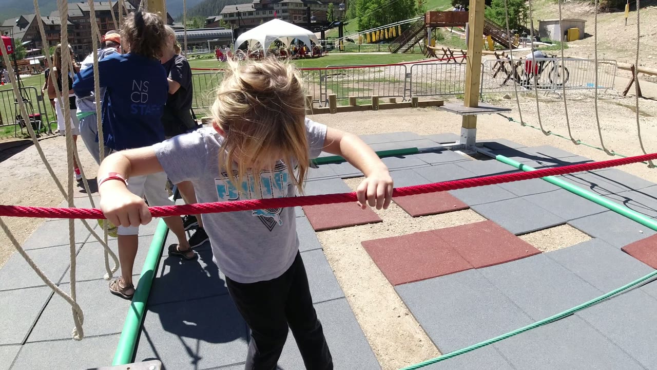 Young girl holding a red rope on a playground balance course.
