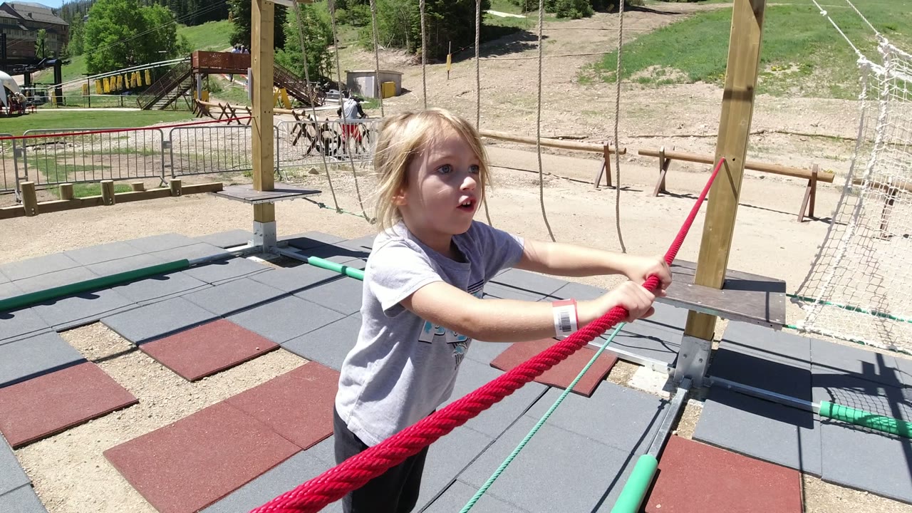 Young girl holding a red rope at an outdoor playground.
