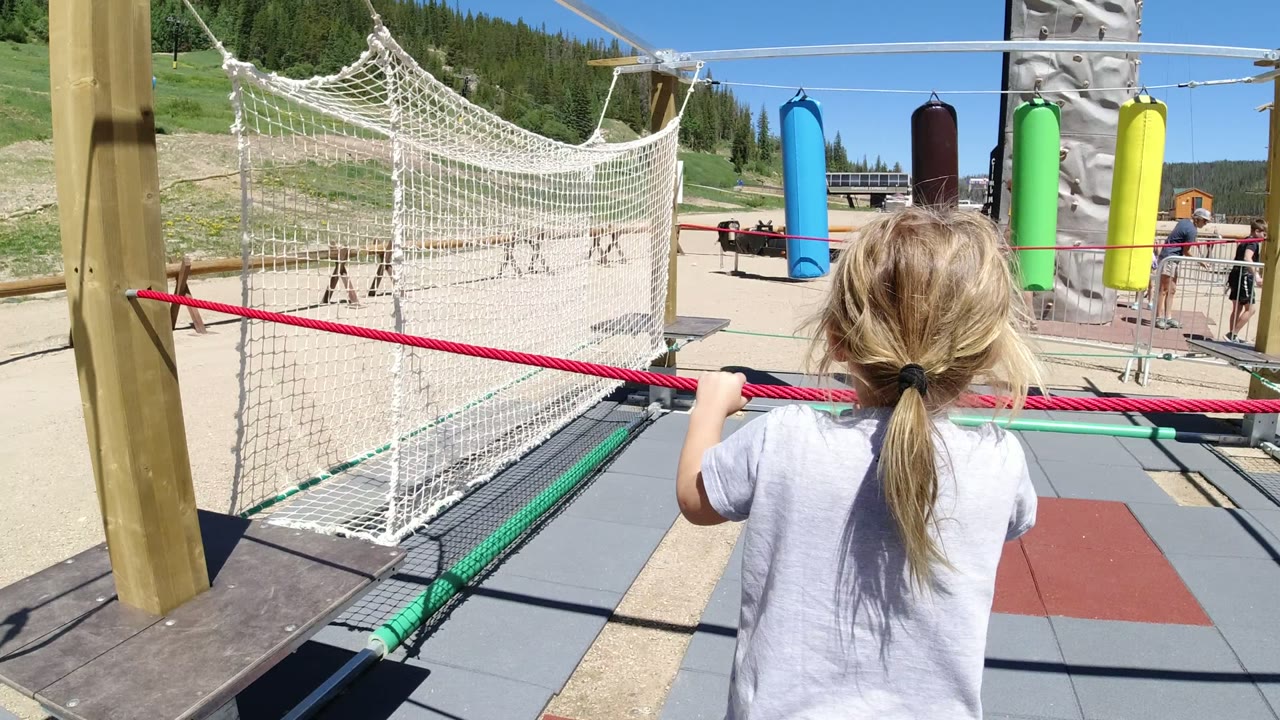 Girl from behind holding a red rope on an outdoor rope course.