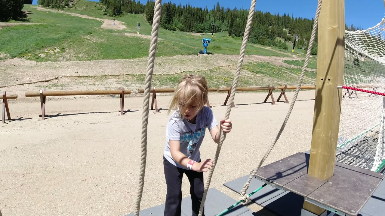 Young girl gripping playground ropes beside a wooden post.