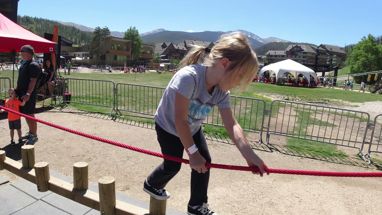 Girl holding a red rope while stepping near wood pegs outdoors.