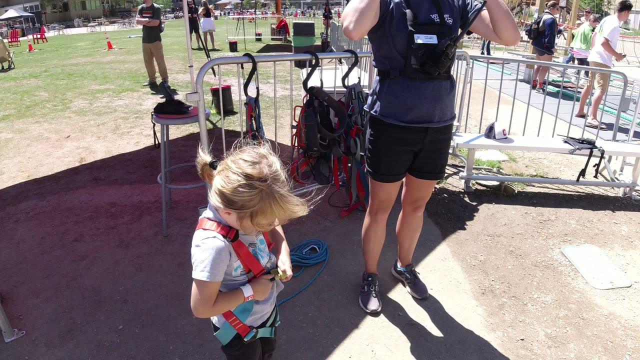Young girl in a red safety harness under a canopy near activity gear.