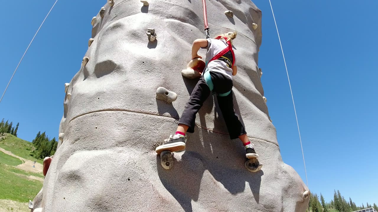 The climber shifts higher on the pale molded wall in Winter Park, Colorado, with her feet spread between holds and the safety rope above her.
