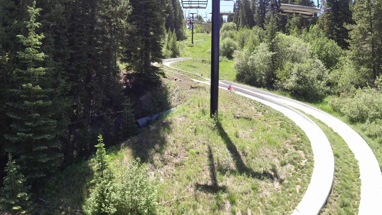 Curving go-kart track through evergreen woods with chairlift towers above.