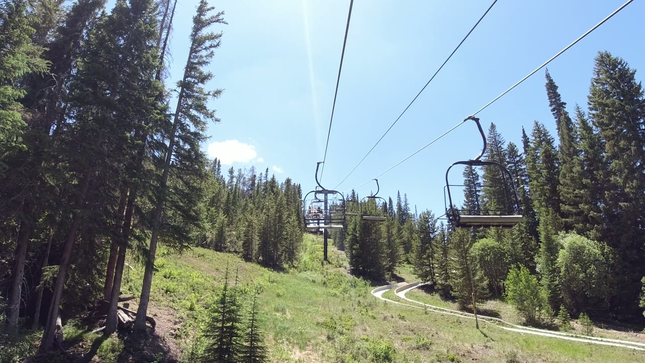 Empty chairlift over a green mountain slope and evergreen trees.