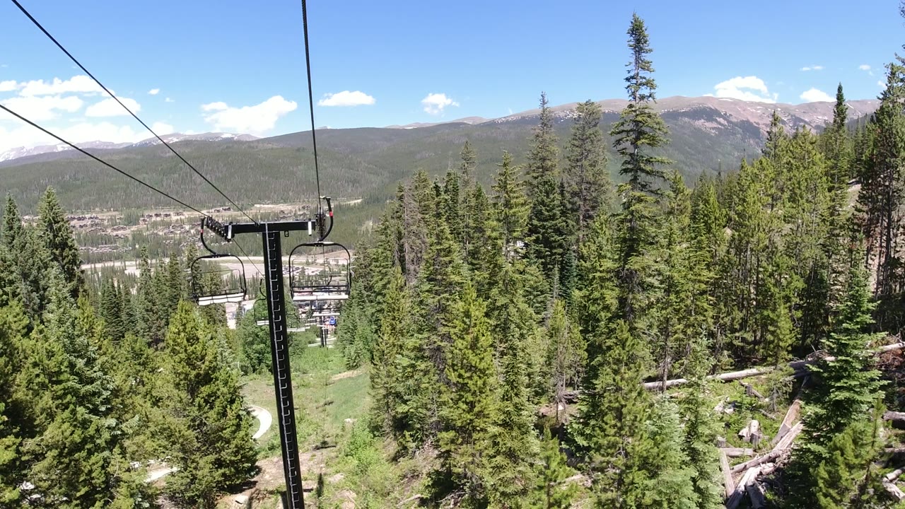 Chairlift cables over evergreen trees with distant mountains and blue sky.