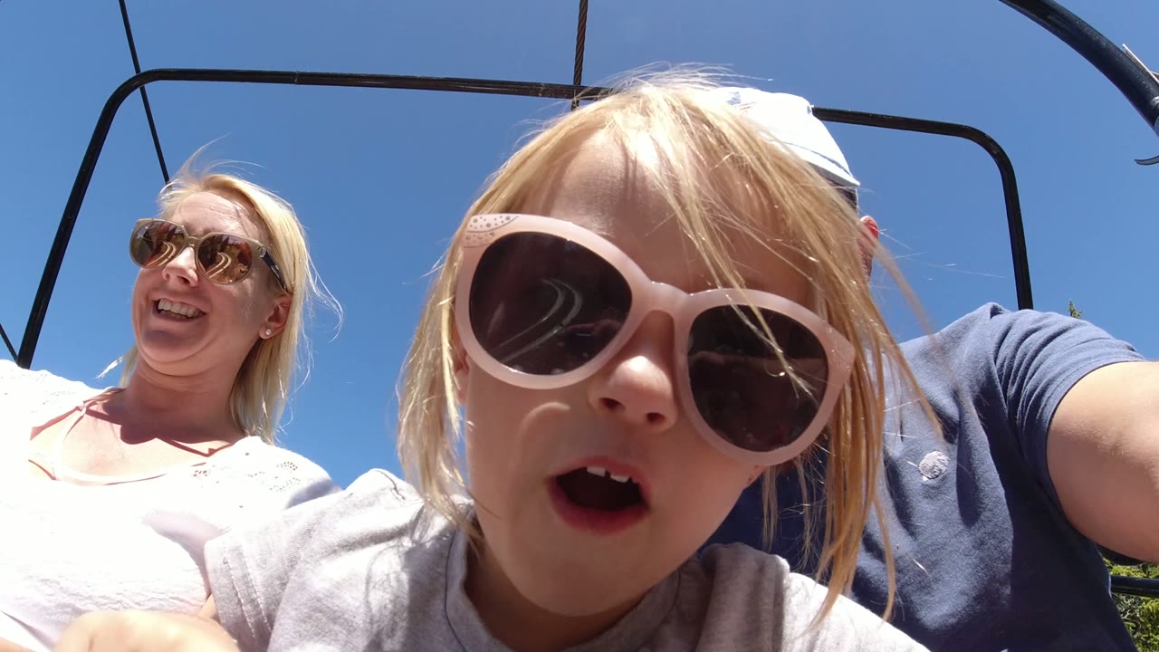 Girl in sunglasses close to camera with parents on chairlift
