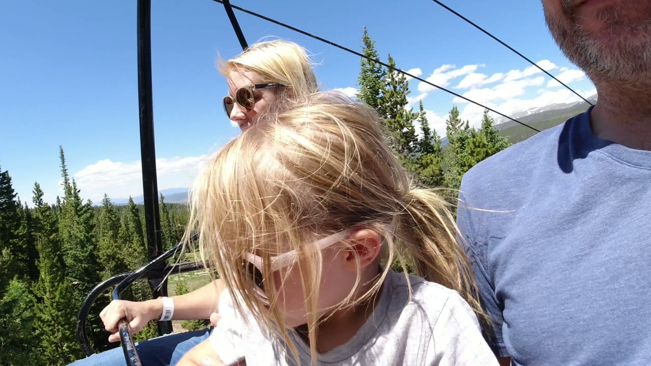 Family members seated on a chairlift above pine trees.