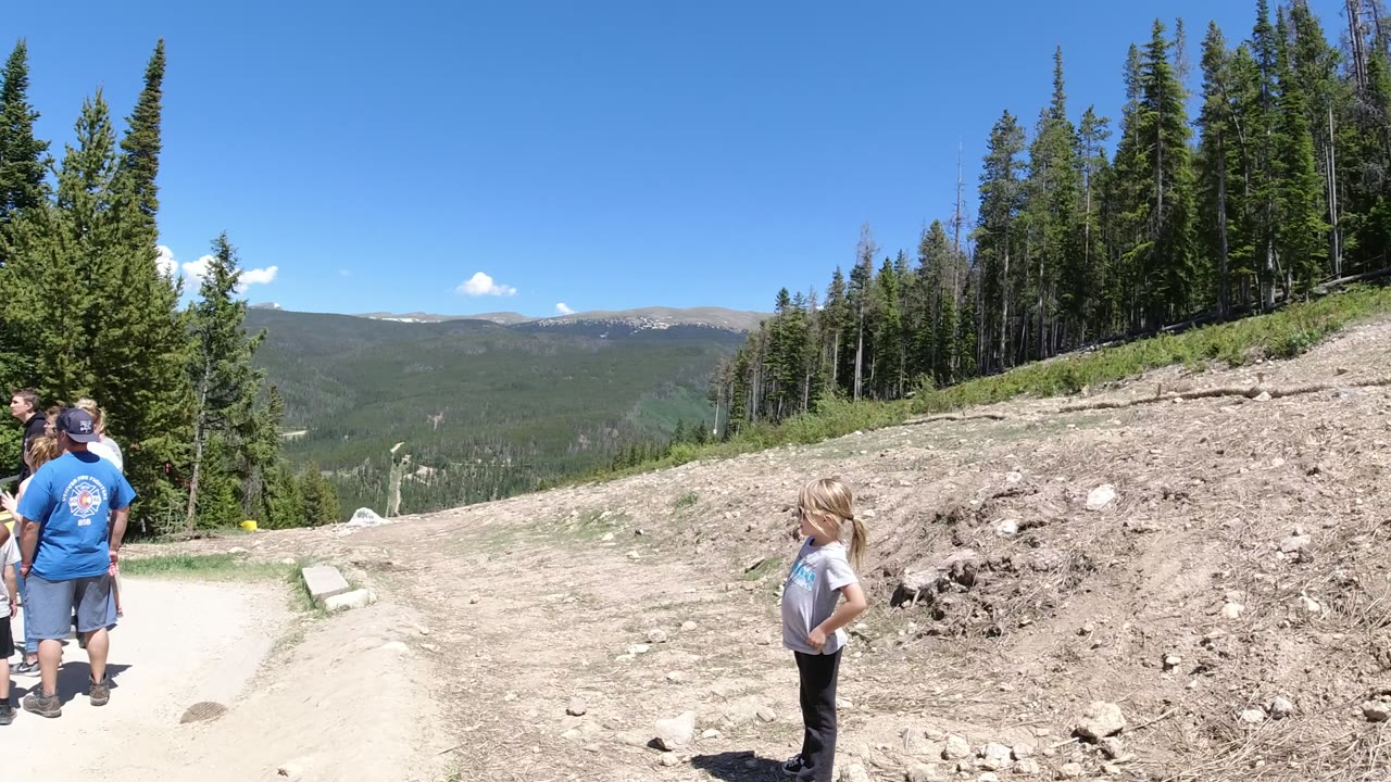 People standing by a gravel path with forest and distant mountains.