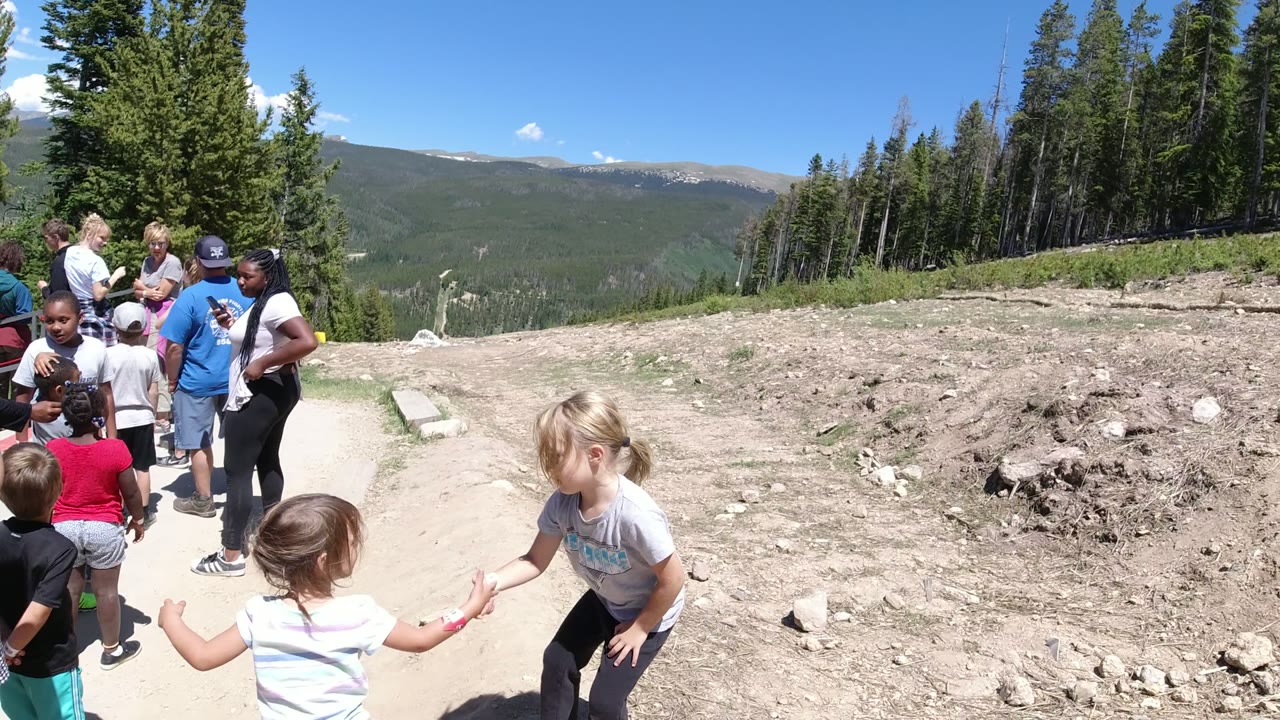 The group remains gathered on the Winter Park, Colorado dirt path, with several children in the foreground and adults standing near the trees in the midground.