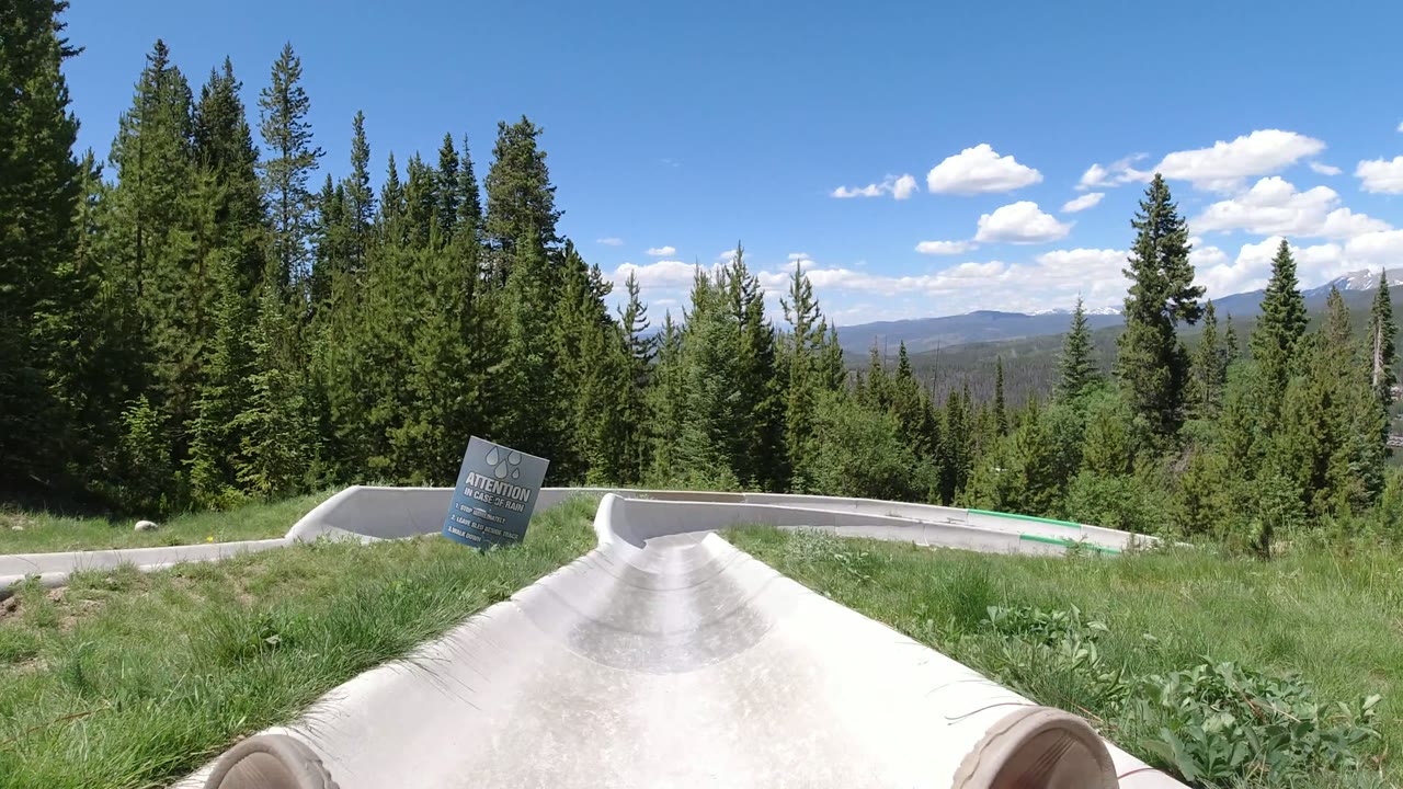 Concrete slide ramp through grass and evergreens with rider feet at the bottom edge.