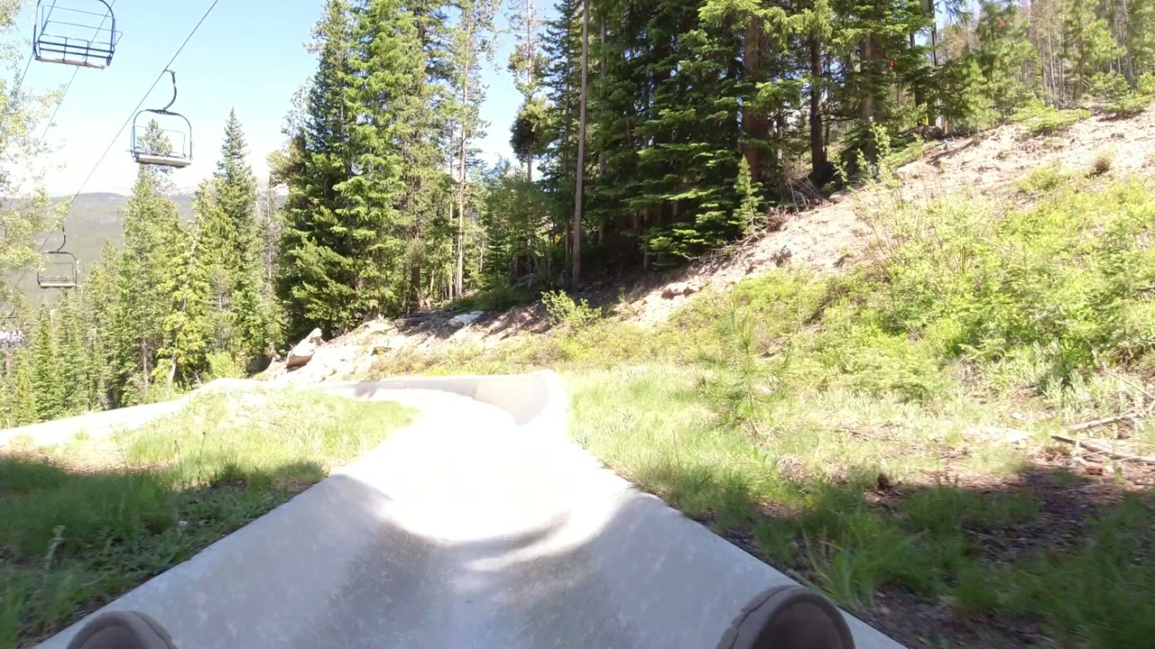 Concrete ramp entering a forested mountain slide with chairlift seats overhead.