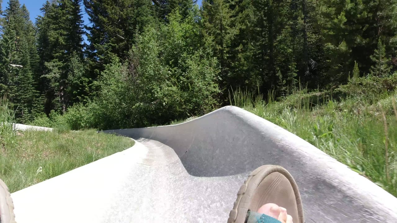 Sandal-clad feet entering a curved stone slide bordered by grass and trees.