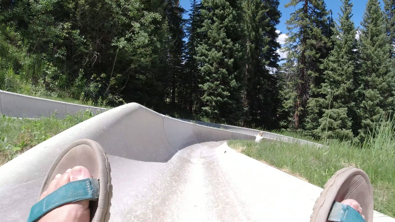 Sandaled feet entering a concrete mountain slide bordered by evergreen trees.