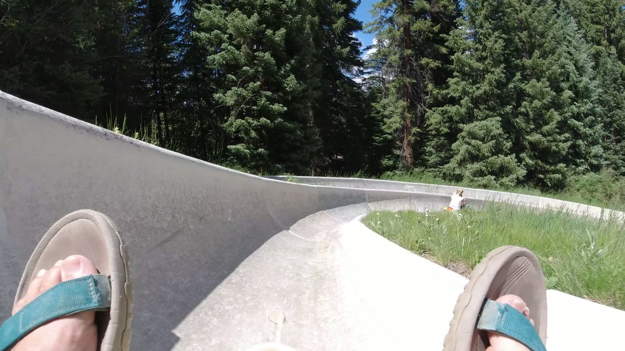 At 0:01 in Winter Park, Colorado, the concrete chute curves across the frame while the rider's sandals remain low in view near grass and tall conifers.