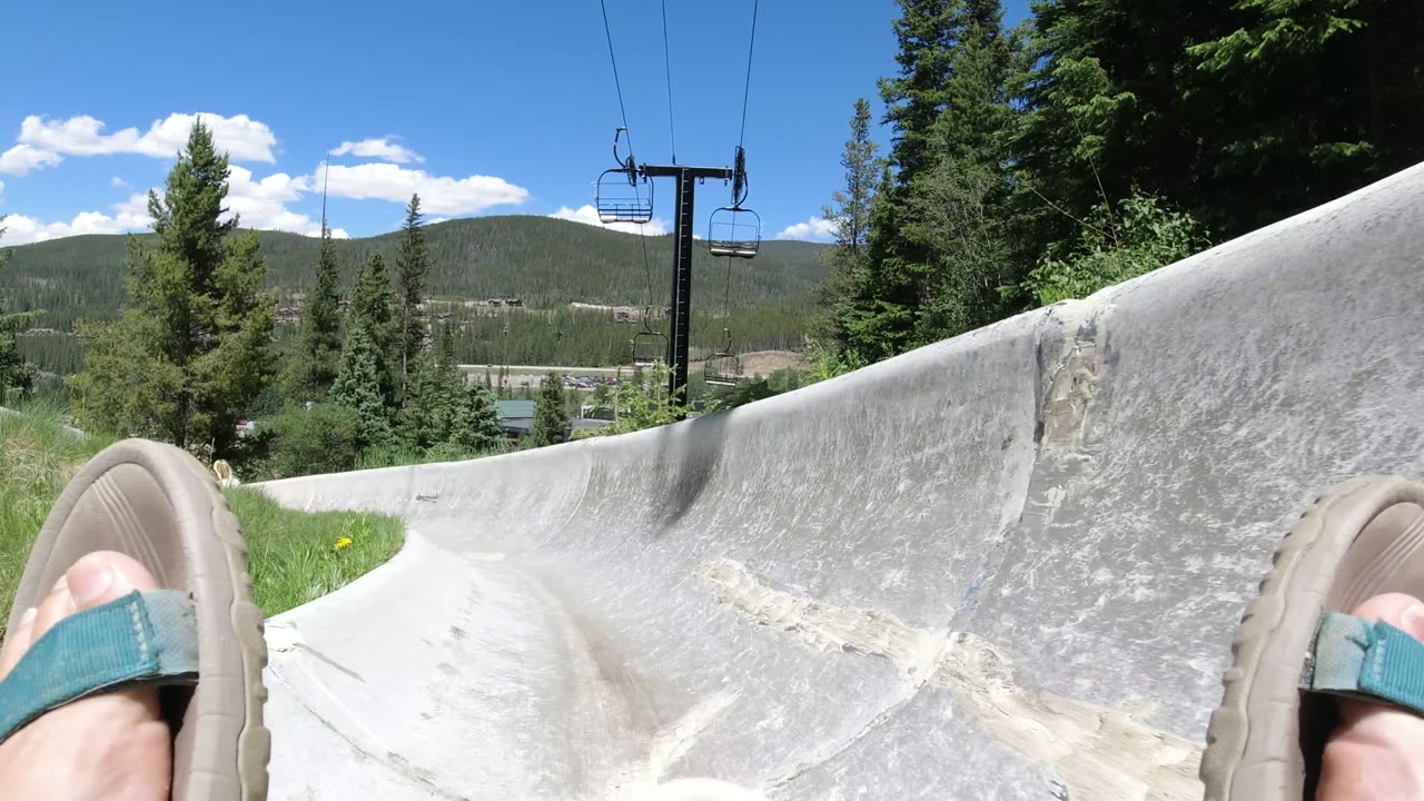 Sandaled feet above a concrete track with chairlift and trees.