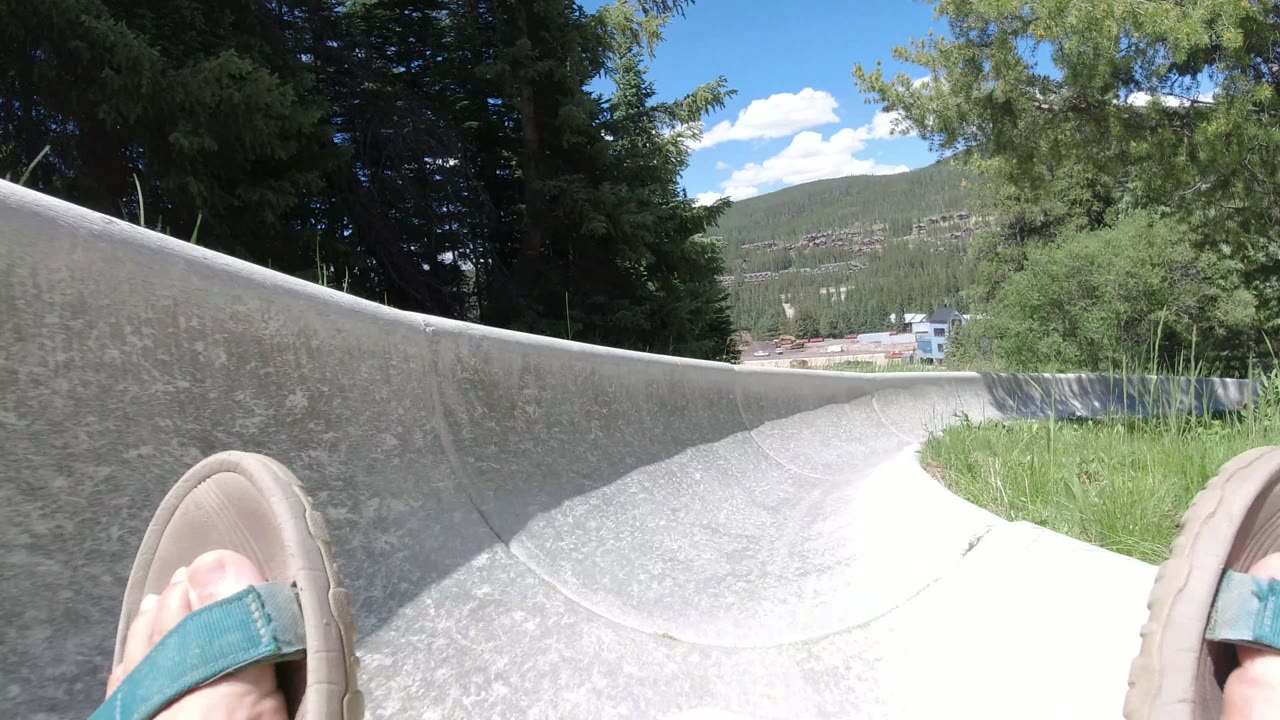 Rider's sandal entering a concrete slide curve with trees and mountains ahead.