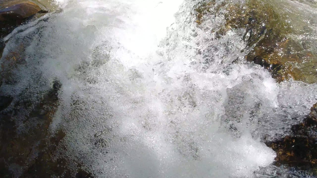 Foaming stream water rushes over dark rocks in Winter Park, Colorado, with bright spray filling most of the frame and no visible people.