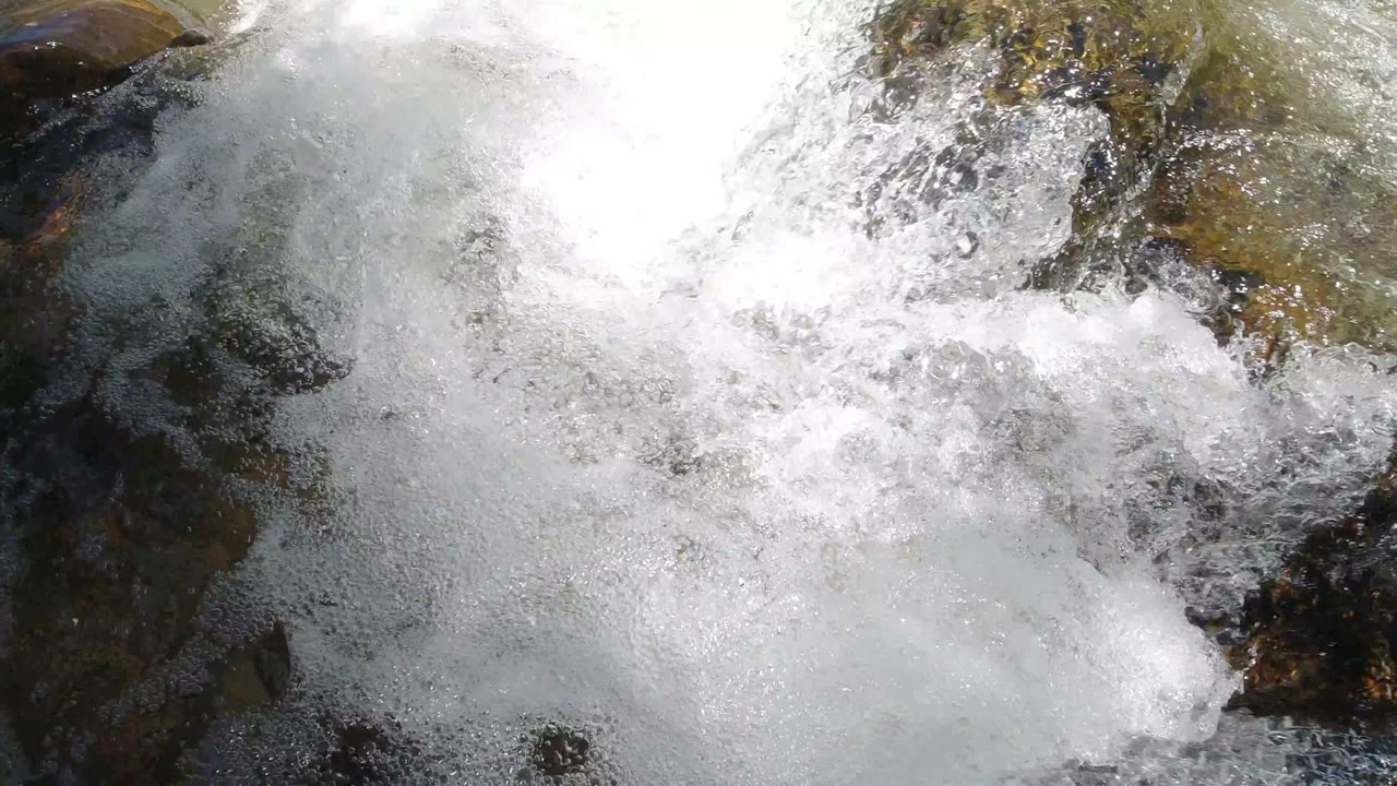Close view of white foam rolling across dark rocks in Winter Park, Colorado, with clear water at the upper edge and no visible people.
