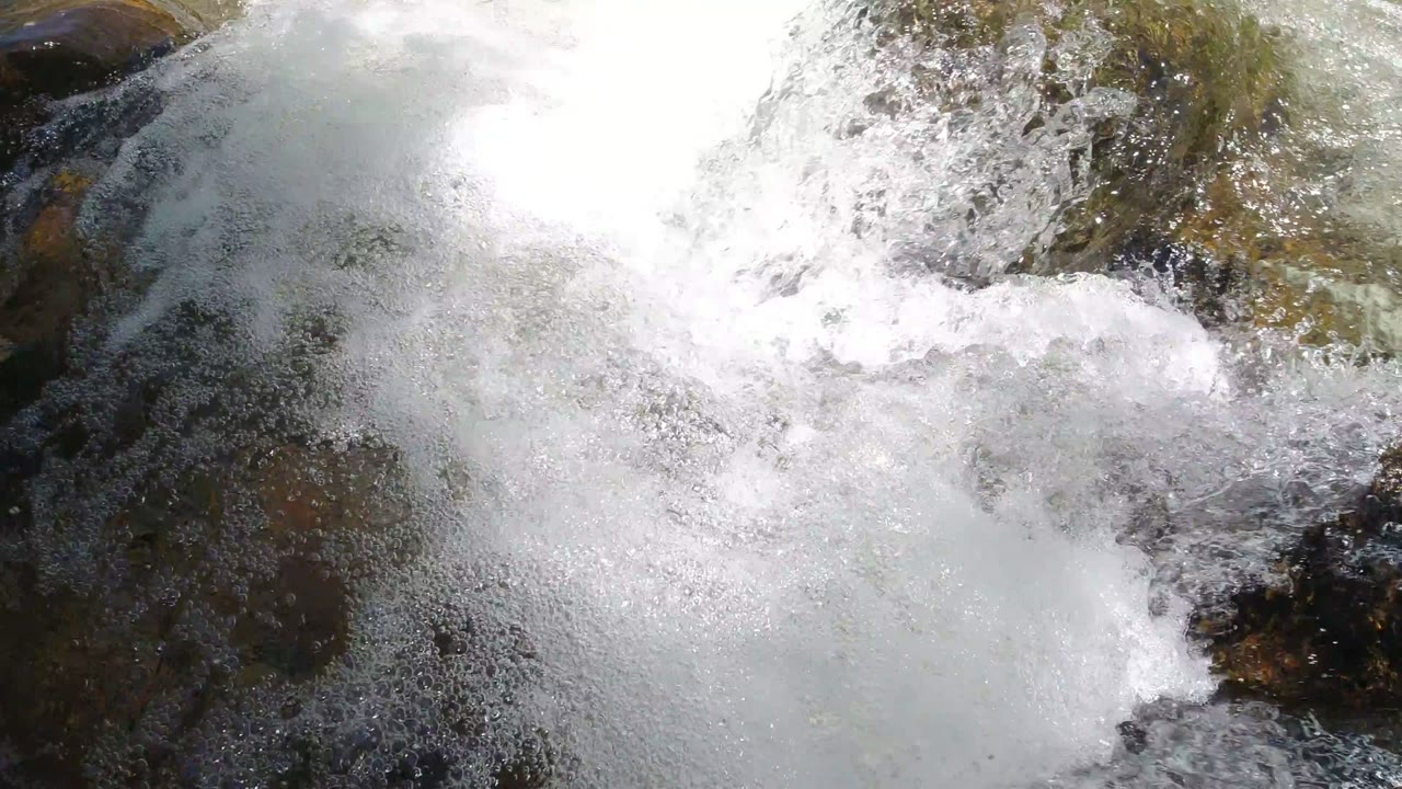 A heavier patch of white river foam fills the lower center while darker wet rock cuts through the current in Winter Park, Colorado, with no visible people.