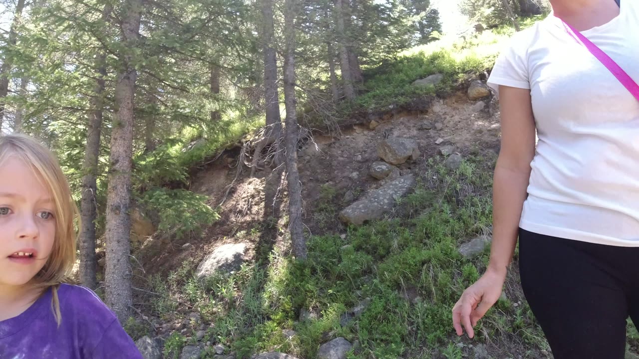The adult woman stands cropped from the neck down while the blonde child appears at the right edge of the forest trail in Winter Park, Colorado.