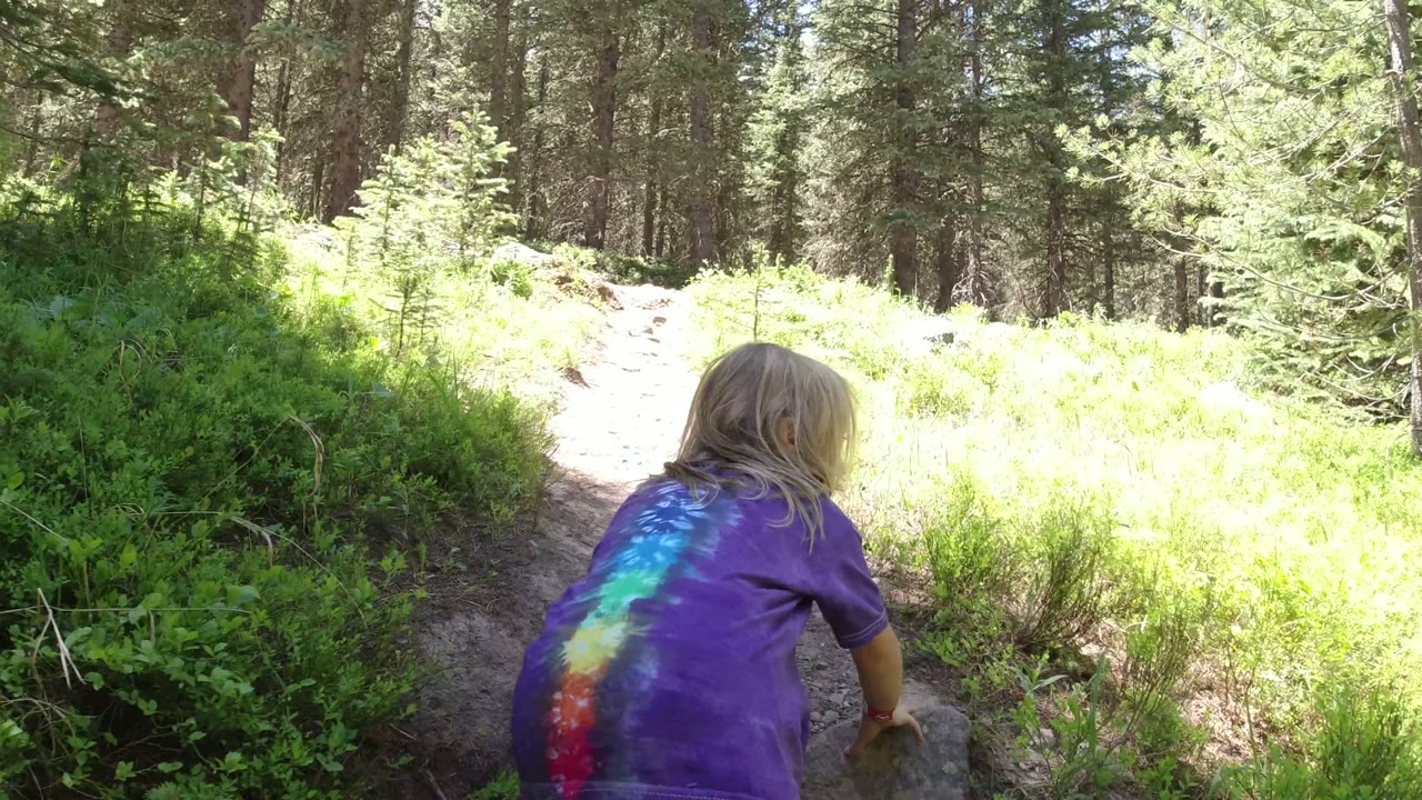 Young girl in a purple tie-dye shirt crawling on a forest trail.