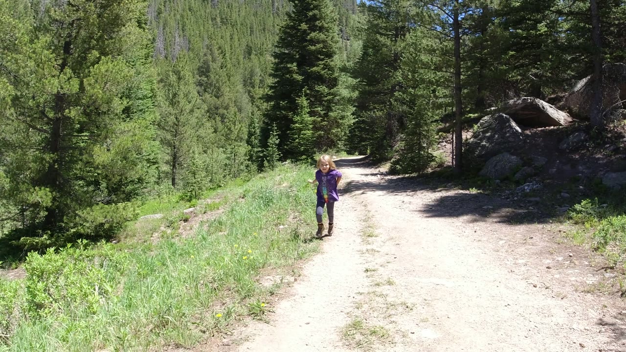 Child running on a dirt forest road surrounded by evergreens.