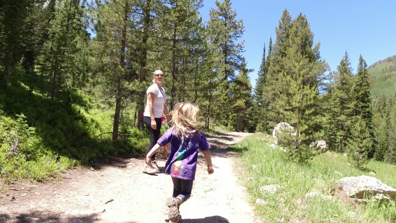 Adult woman and young girl on a sunny forest trail.