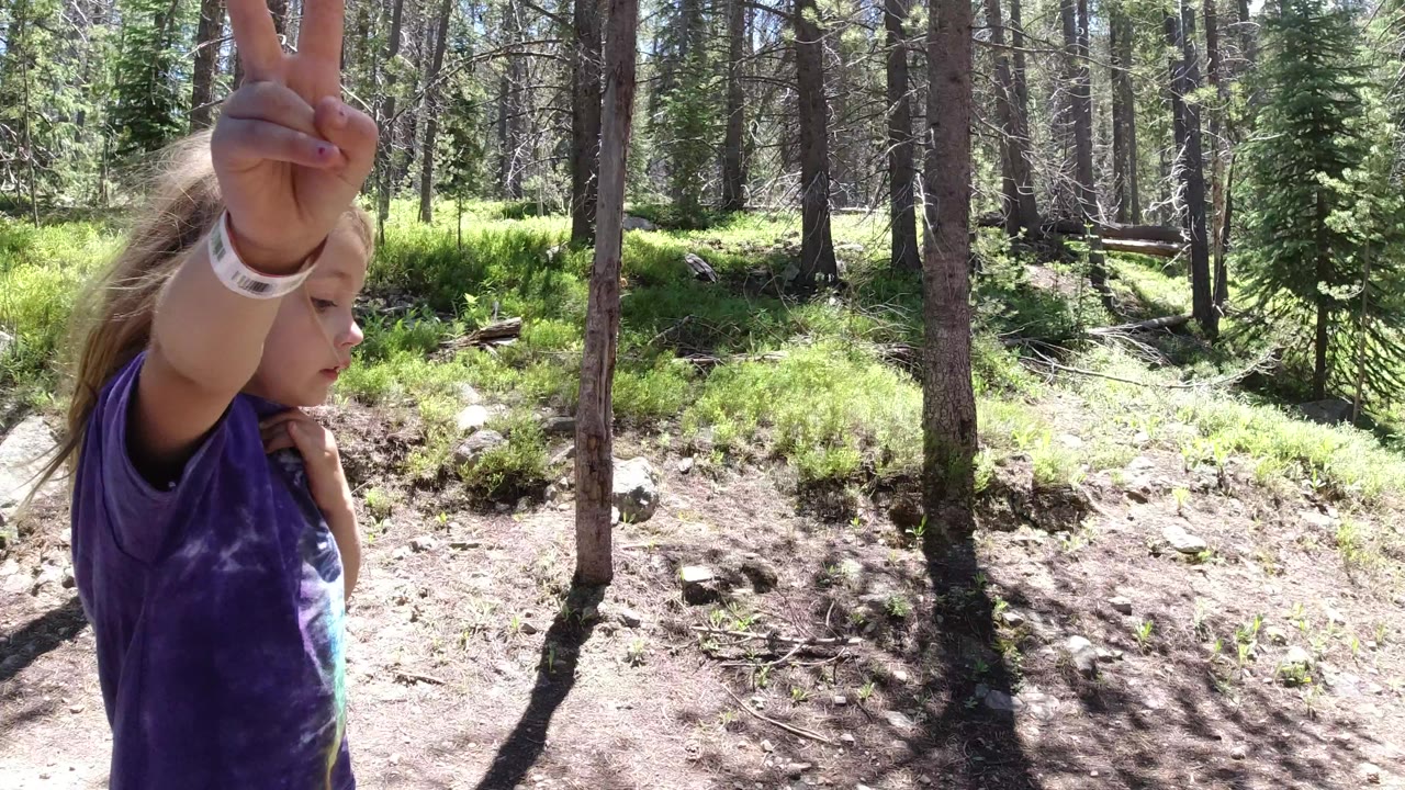 One second in, the child remains partly cropped on the left with an arm raised, while the Winter Park forest floor, rocks, and upright tree trunks dominate the frame.