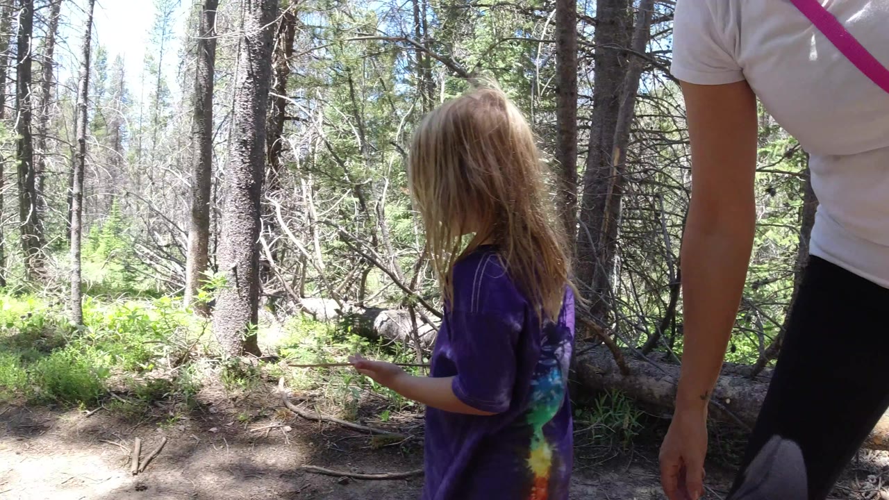 The girl holds a small stick or twig on the Winter Park, Colorado trail as the adult remains partly cropped in the foreground.