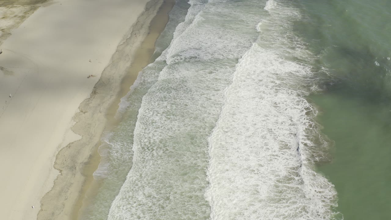 Overhead view of white surf crossing pale sand and green-blue water in Los Cabos, Mexico, with no visible people in this frame.