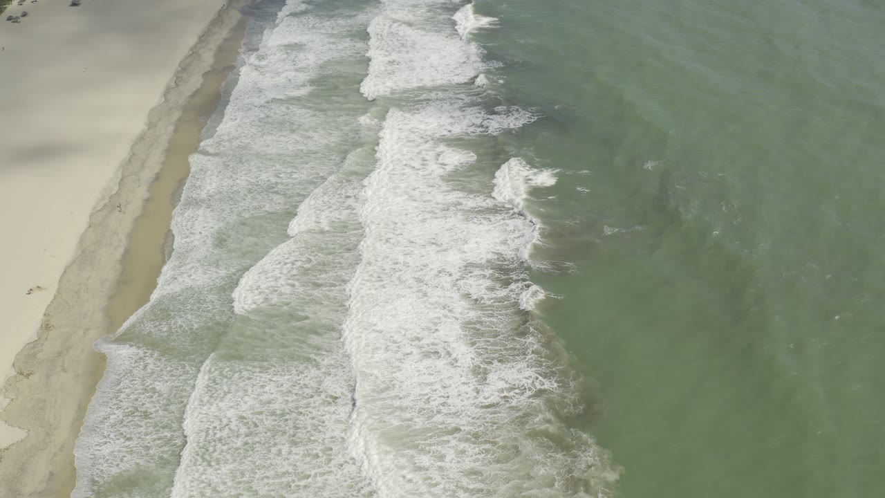 Aerial Los Cabos beach view with several bands of white surf crossing toward the sand, muted green water, and no visible people in frame.
