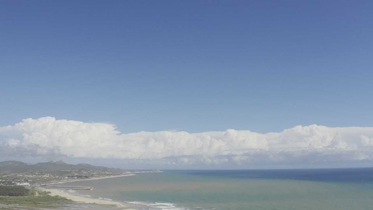 Wide aerial coastline under blue sky and large clouds.