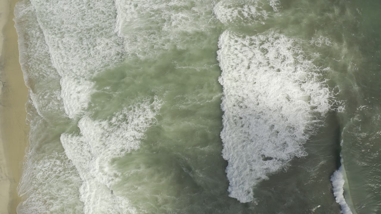 Overhead green surf breaking across pale sand.