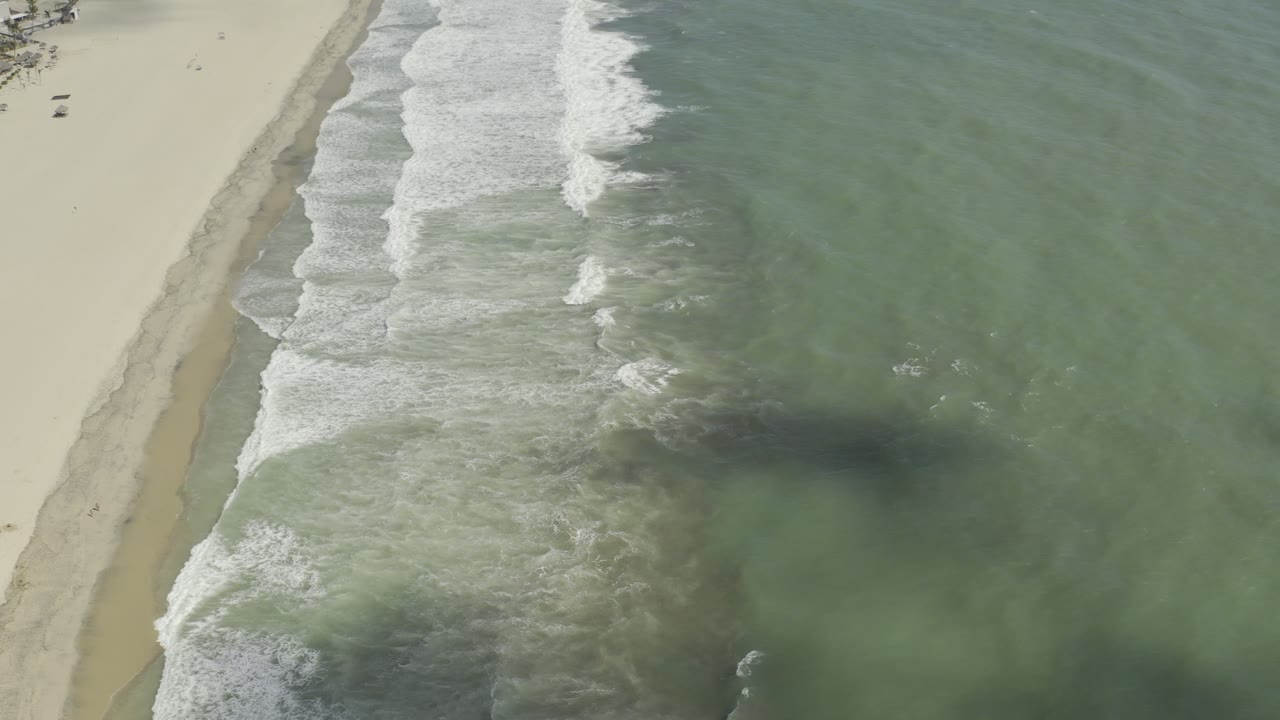 Drone-style view of surf breaking along a quiet beach.