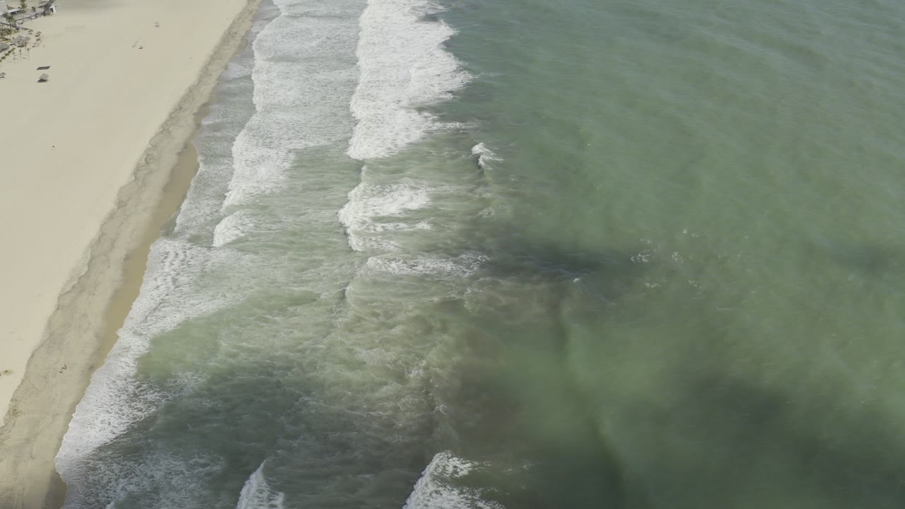 Overhead beach with green water and white surf on sand.