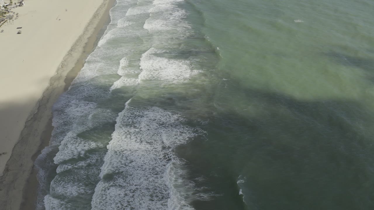 Green ocean water covers most of the frame with surf breaking near the beach.