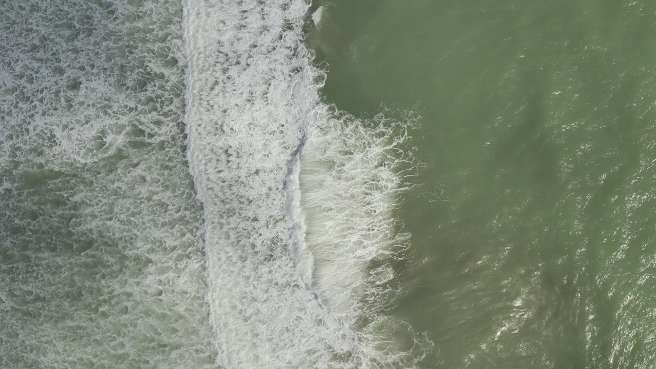Top-down view of green-gray ocean in Los Cabos, Mexico, with a vertical band of white surf and no visible people.