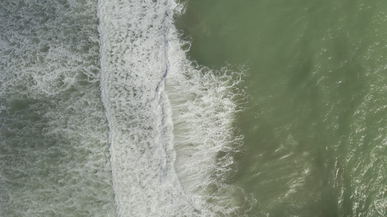 Foamy wave edge beside darker rough water and green sea.