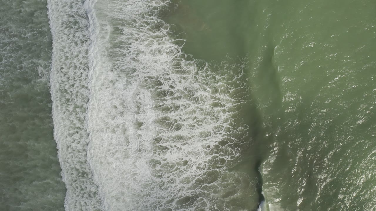 Top-down view of green seawater in Los Cabos, Mexico, with a wide vertical line of white surf foam and no visible people.